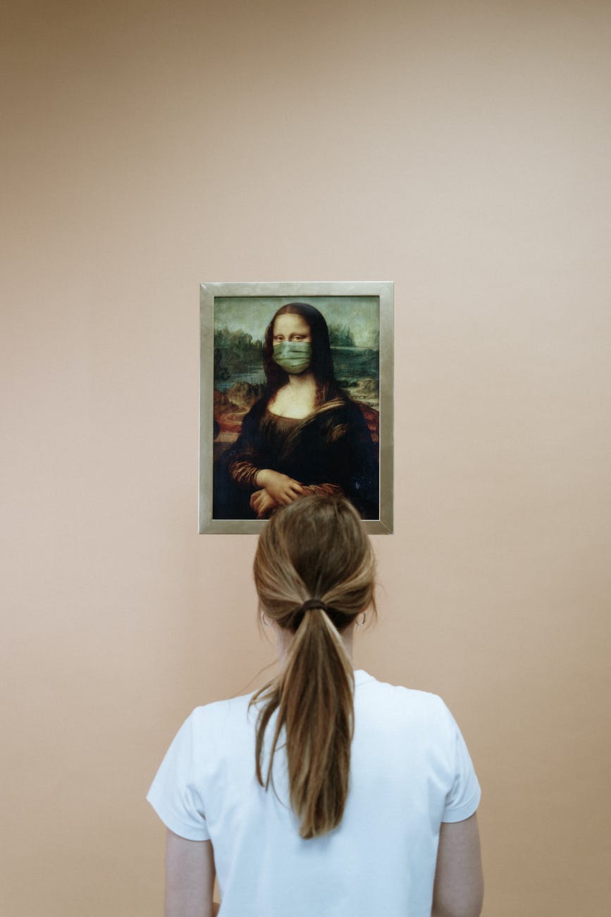 woman in white shirt looking at a painting of mona lisa with face mask