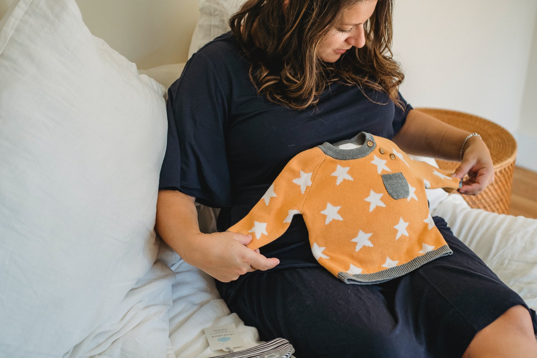 crop expectant woman with baby wear on bed in house