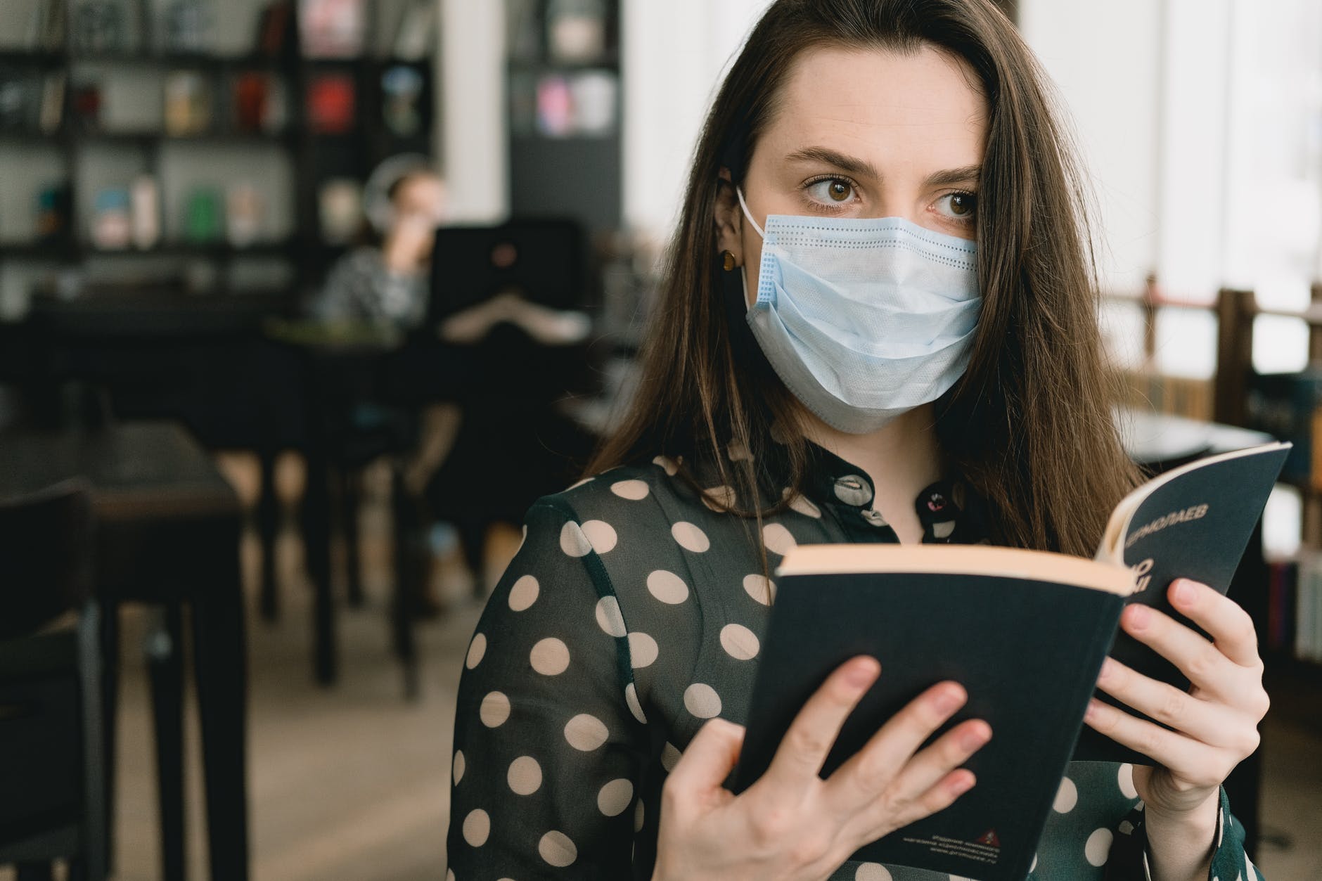 young woman in protective mask reading book in library
